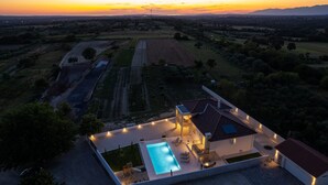 Une maison moderne dotée d’une piscine, d’un espace salon extérieur et offrant une vue sur le coucher de soleil au-dessus des champs.