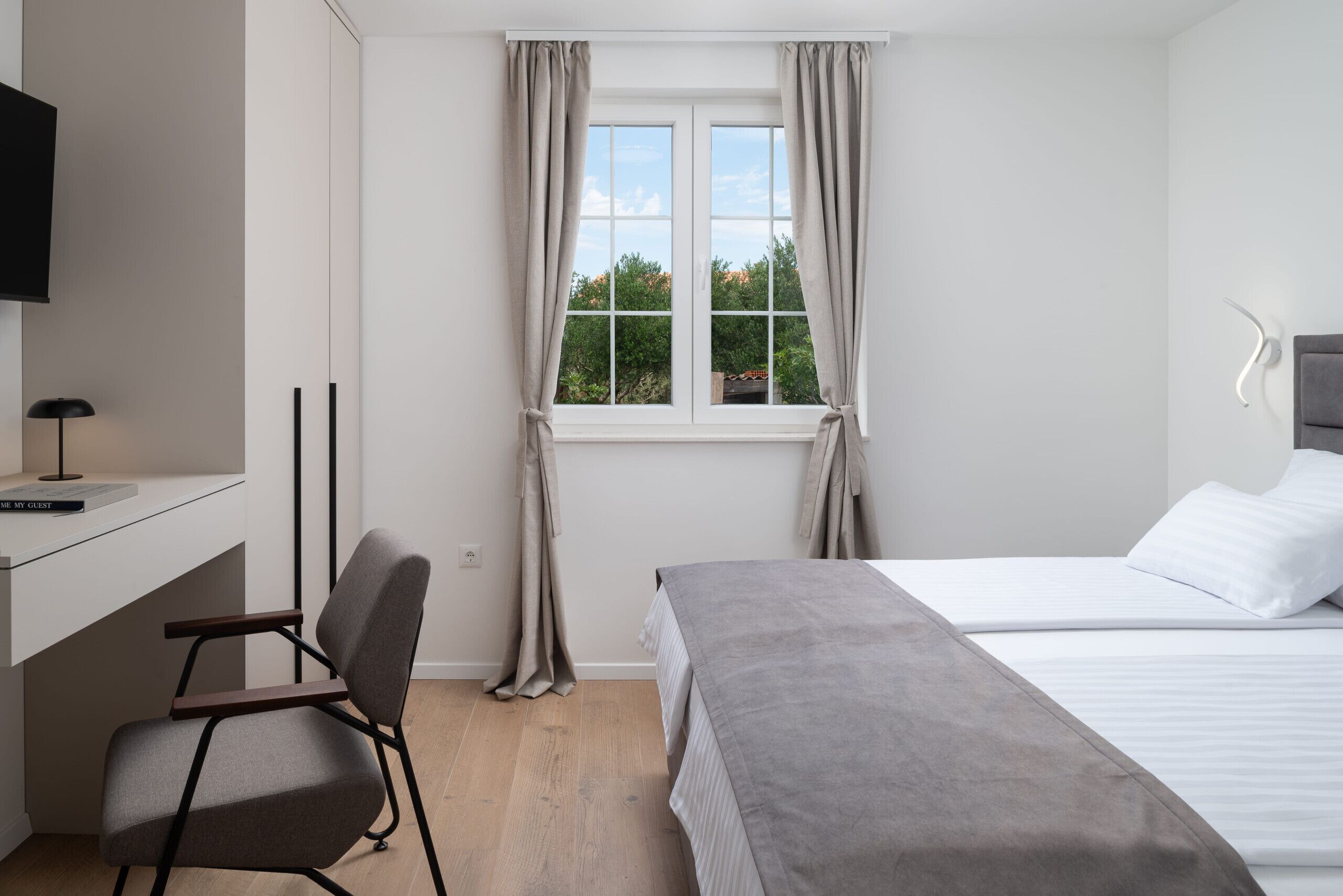 Un dormitorio con cama, un escritorio con silla, un televisor y una ventana con cortinas.