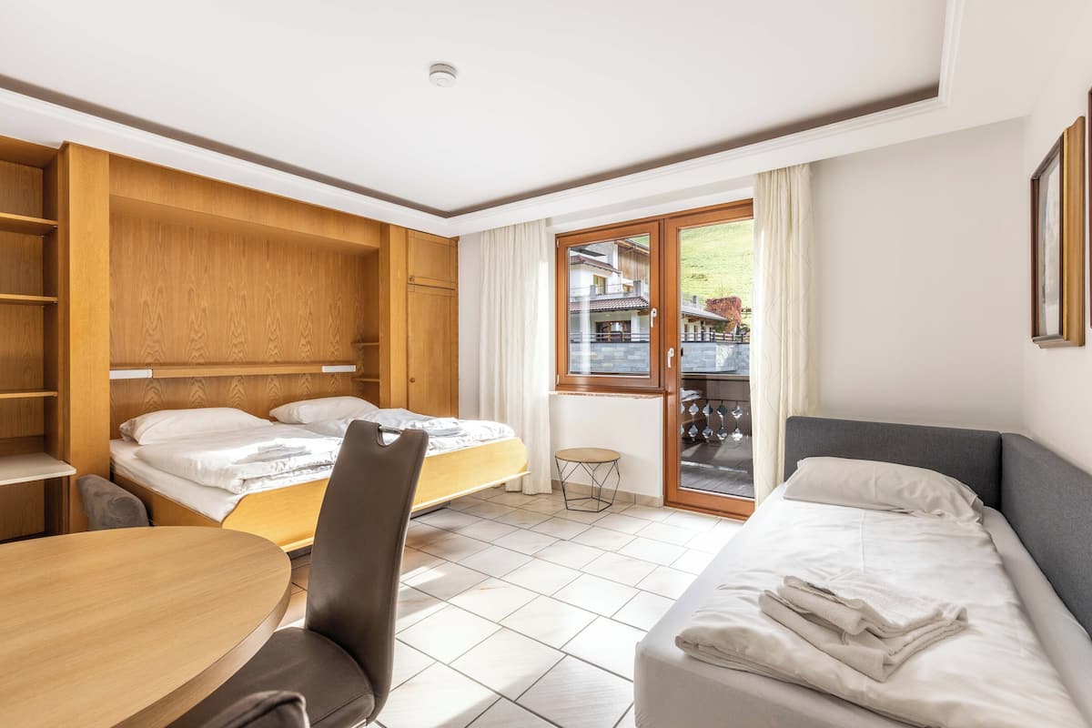 Una habitación de hotel con una cama, un sofá, una mesita y una silla. Hay una ventana con cortinas y vistas a un edificio.