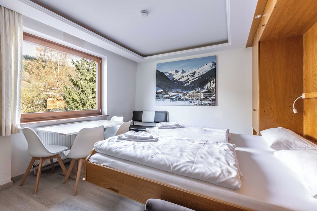 Habitación de hotel con una cama, un escritorio y una silla. Se ve un ventanal con vistas a árboles y montañas.