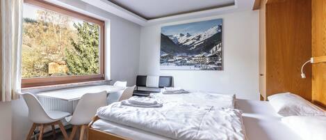 A hotel room with a bed, a desk, and a chair. There is a window with a view of trees and mountains.