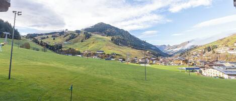 A view of a town nestled in a valley with green fields and mountains in the background.