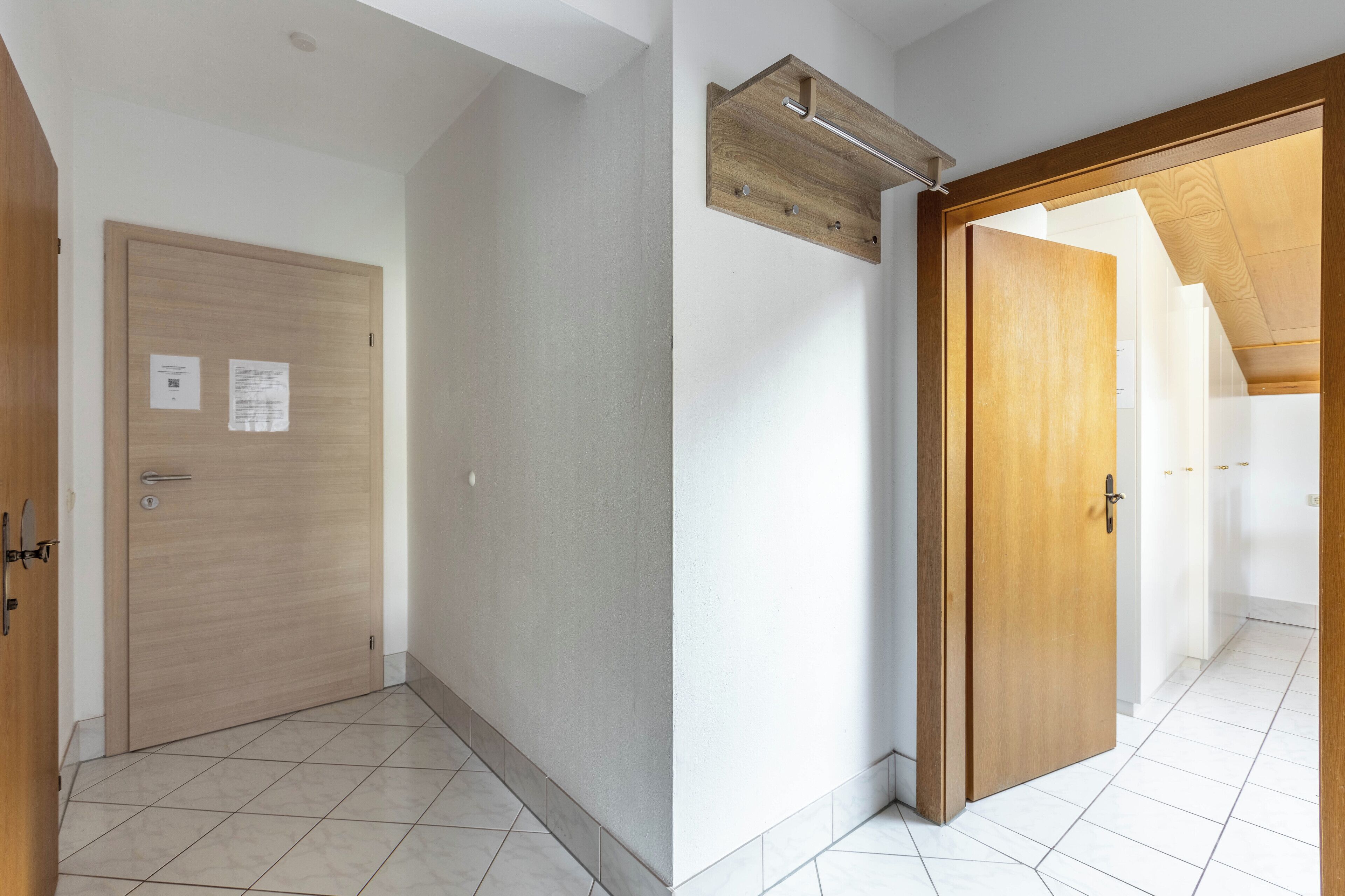 A hallway with a wooden door, a white wall, and a tiled floor.