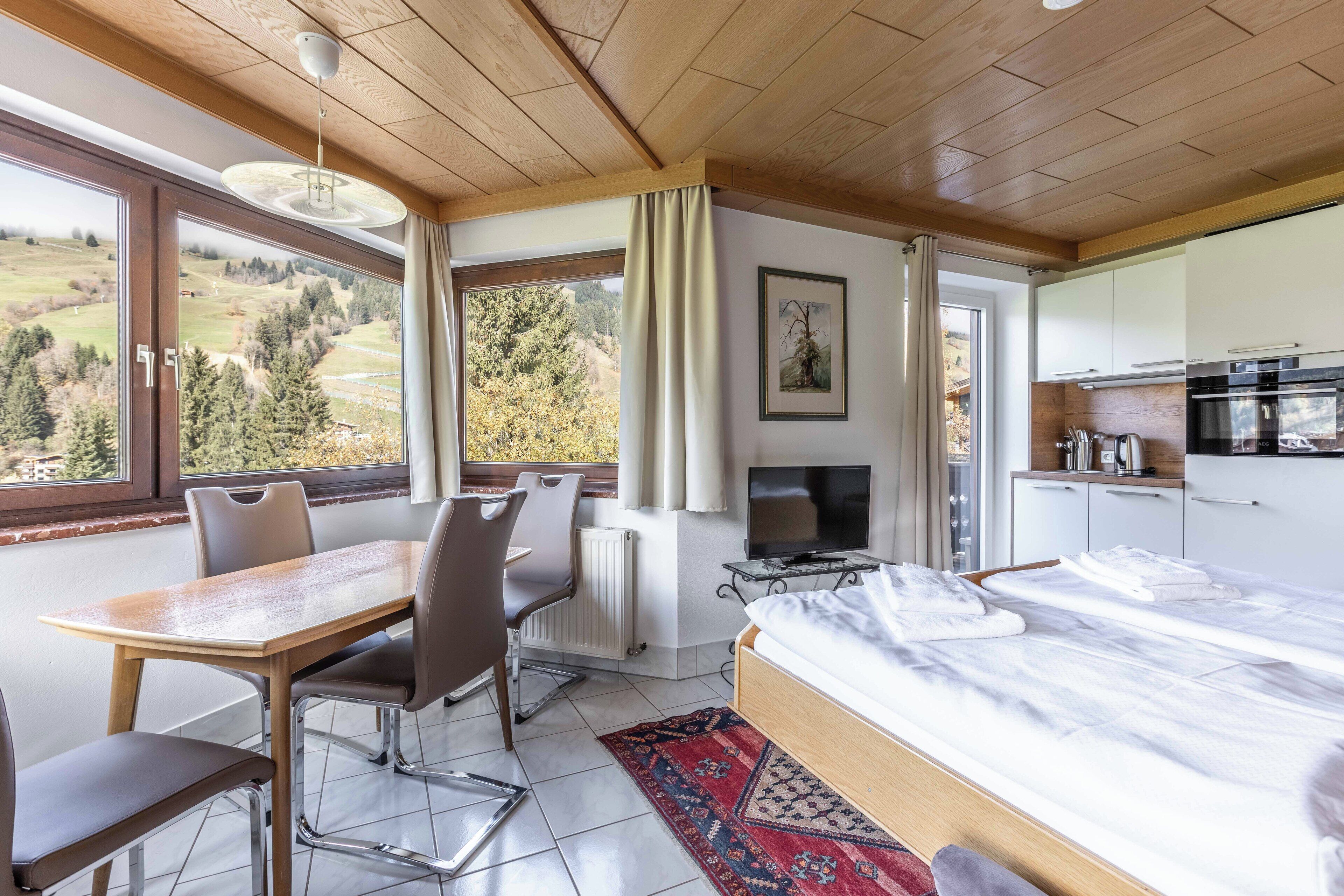 Een slaapkamer met een bed, een televisie, een eettafel met stoelen en uitzicht op de omgeving.