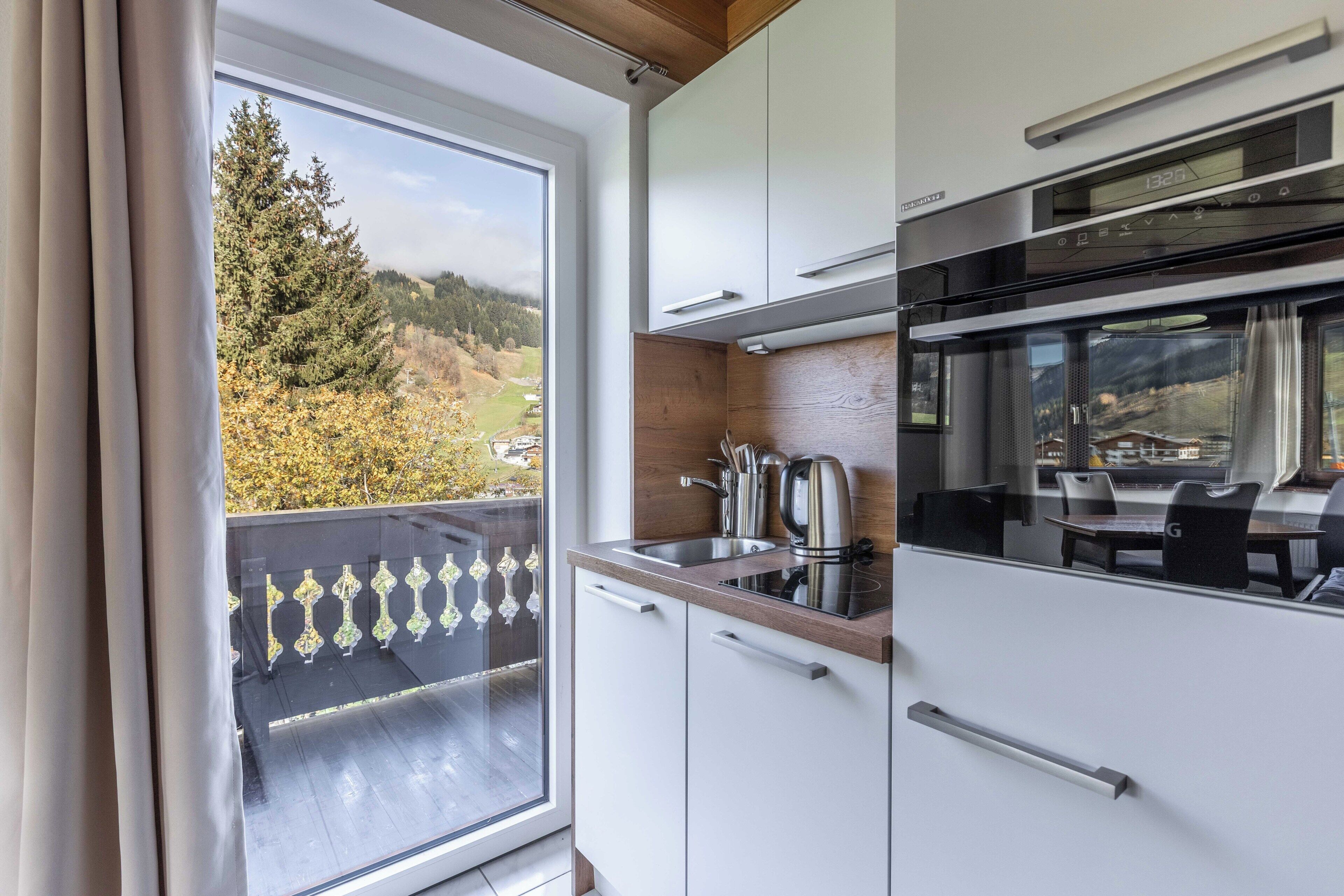 A modern kitchen with white cabinets, a stainless steel sink, and a view of a balcony with a glass door.