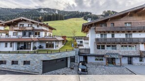 Une vue sur un village de montagne avec des bâtiments de style chalet traditionnel, une cour pavée et une colline verdoyante en arrière-plan.