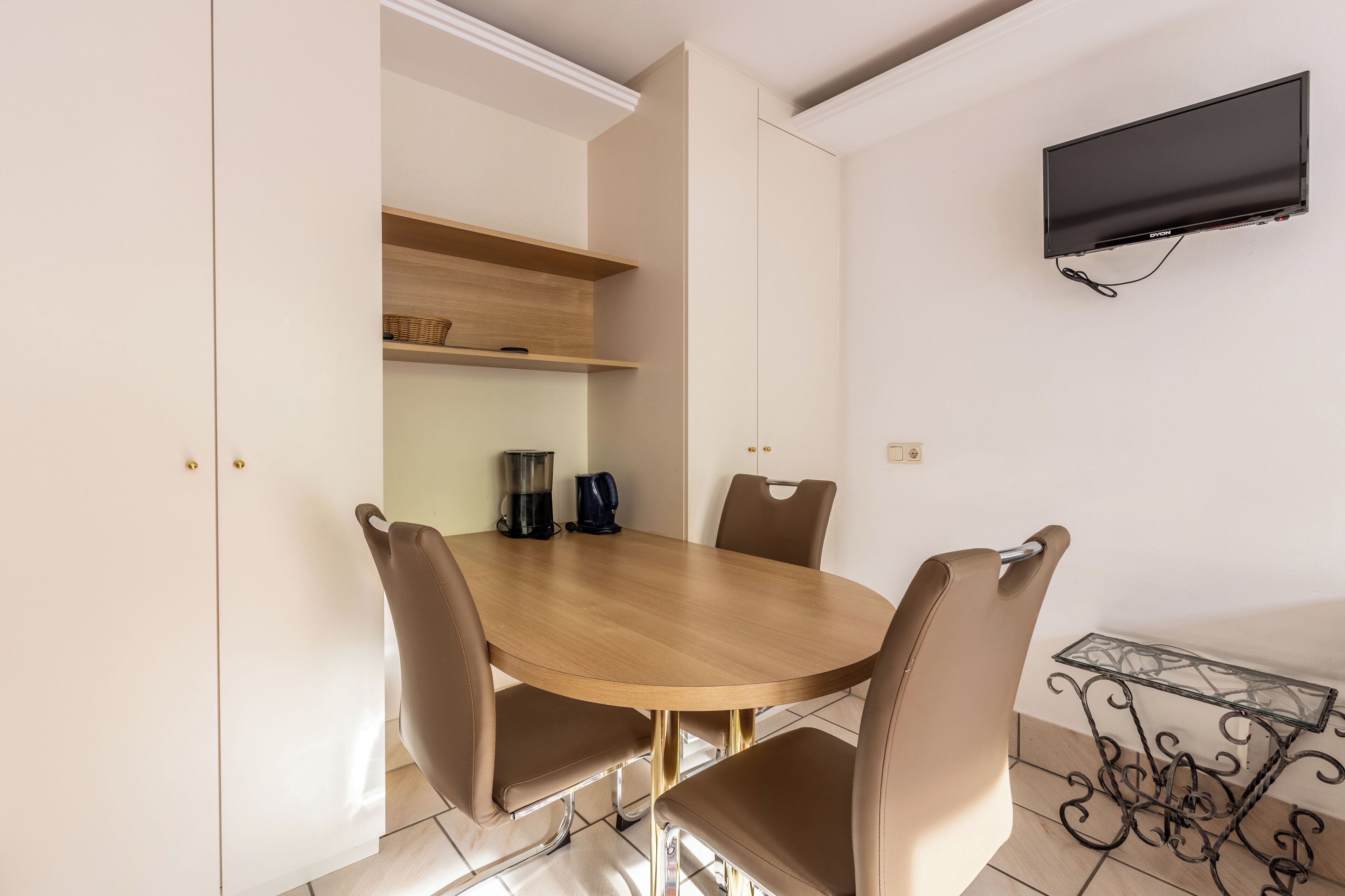 Un coin repas comprenant une table ronde, quatre chaises, une machine à café et un téléviseur fixé au mur.