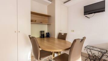Un coin repas comprenant une table ronde, quatre chaises, une machine à café et un téléviseur fixé au mur.