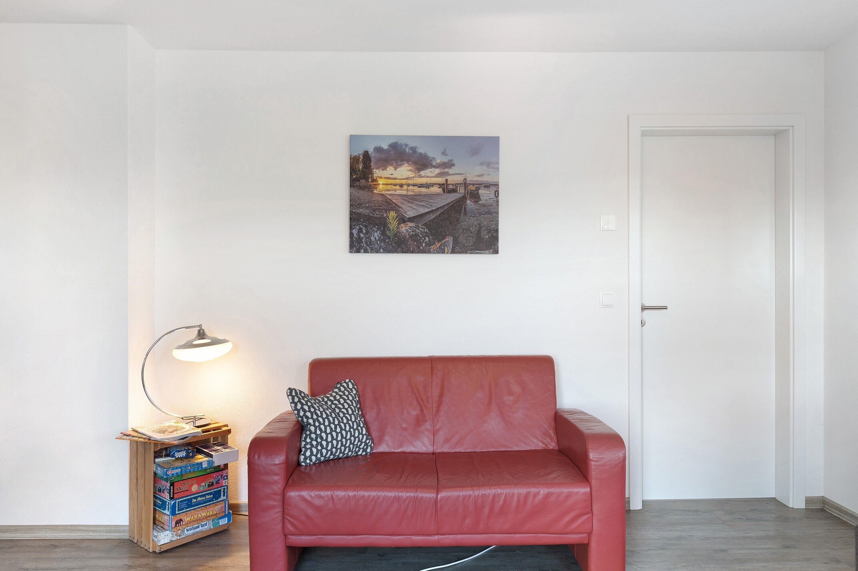 A red leather sofa, a small side table with a lamp, and a picture on the wall.