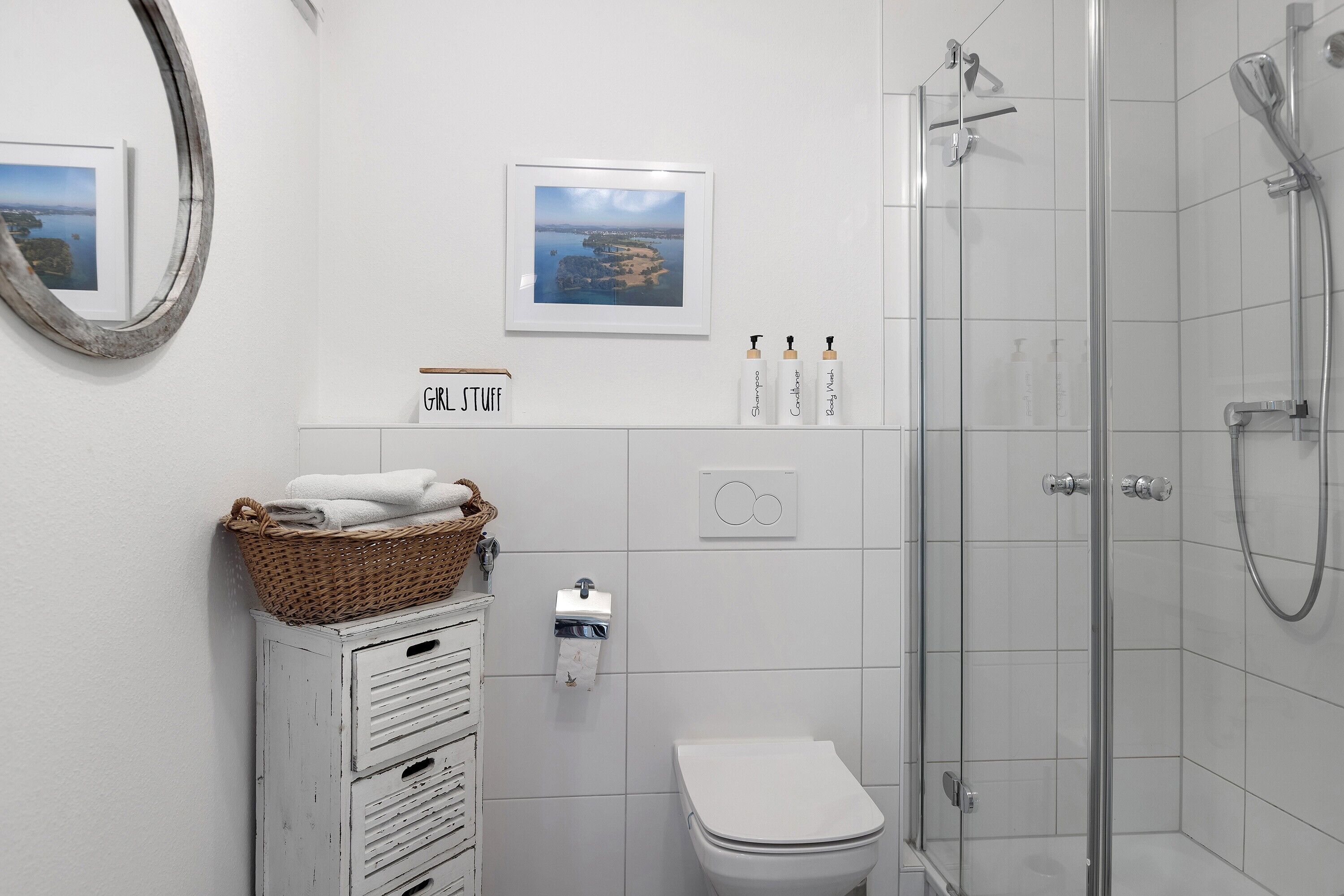 Une salle de bain équipée d’une douche, de toilettes et d’un panier fixé au mur contenant des serviettes.