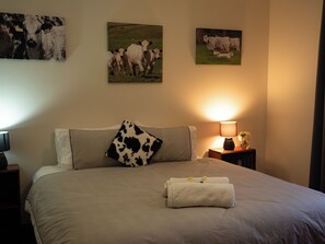 Habitación de hotel con cama, mesita de noche con lámpara y un cuadro con vacas.