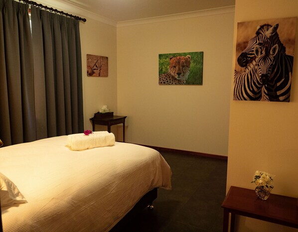 A hotel room with a bed, a small table with a tissue box, and two animal-themed paintings on the wall.