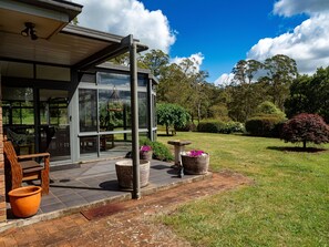 A modern house with large glass windows, a patio with outdoor furniture, and a well-maintained garden with various plants and a birdbath.