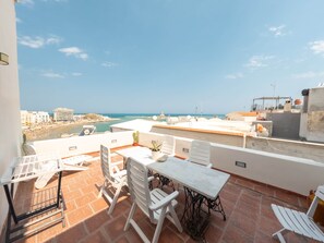 Una terraza con una mesa y sillas, una planta en maceta y vistas a la playa y al paisaje urbano.