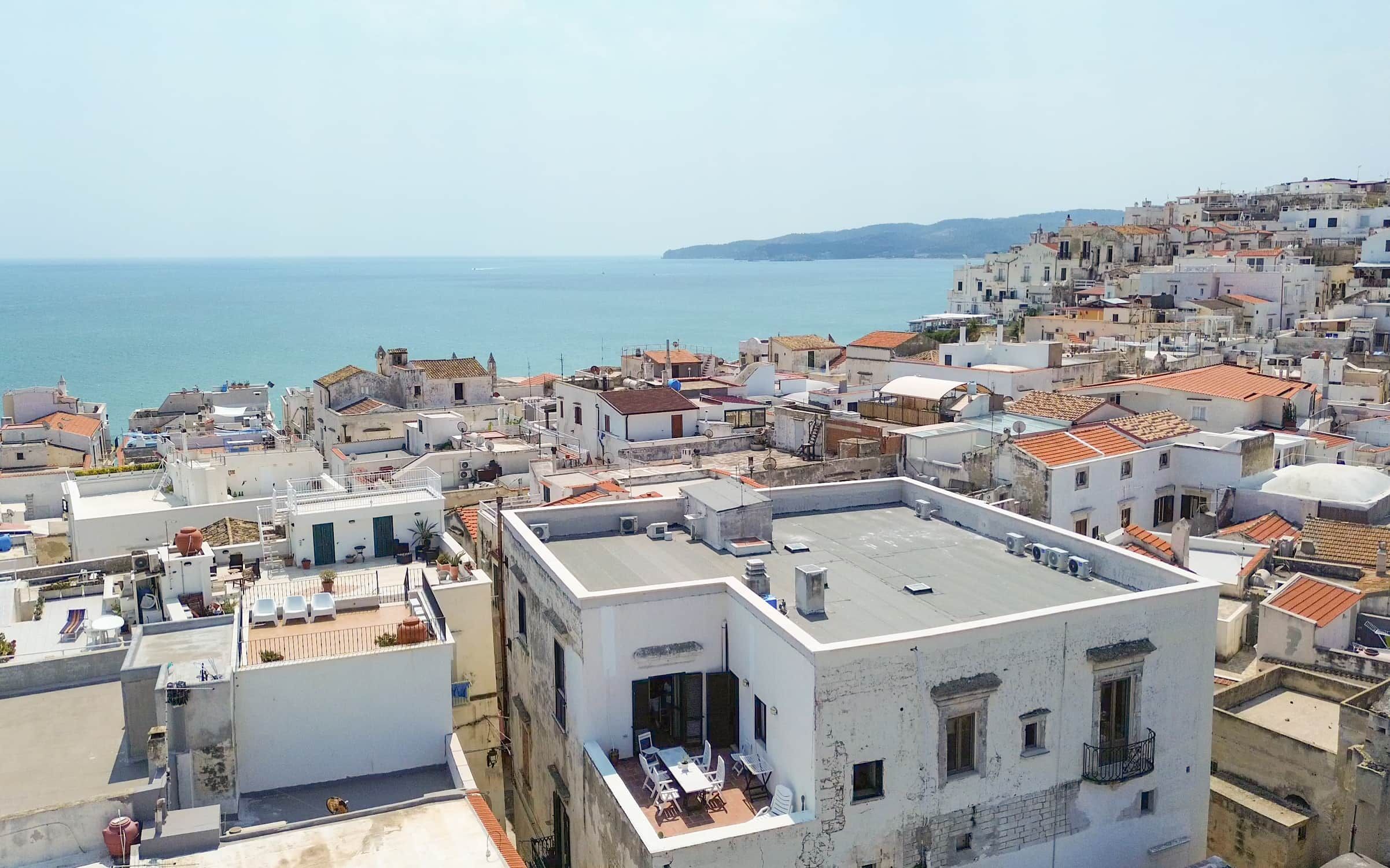 Un paisaje urbano costero con edificios blancos, techos de tejas rojas y vistas al mar.
