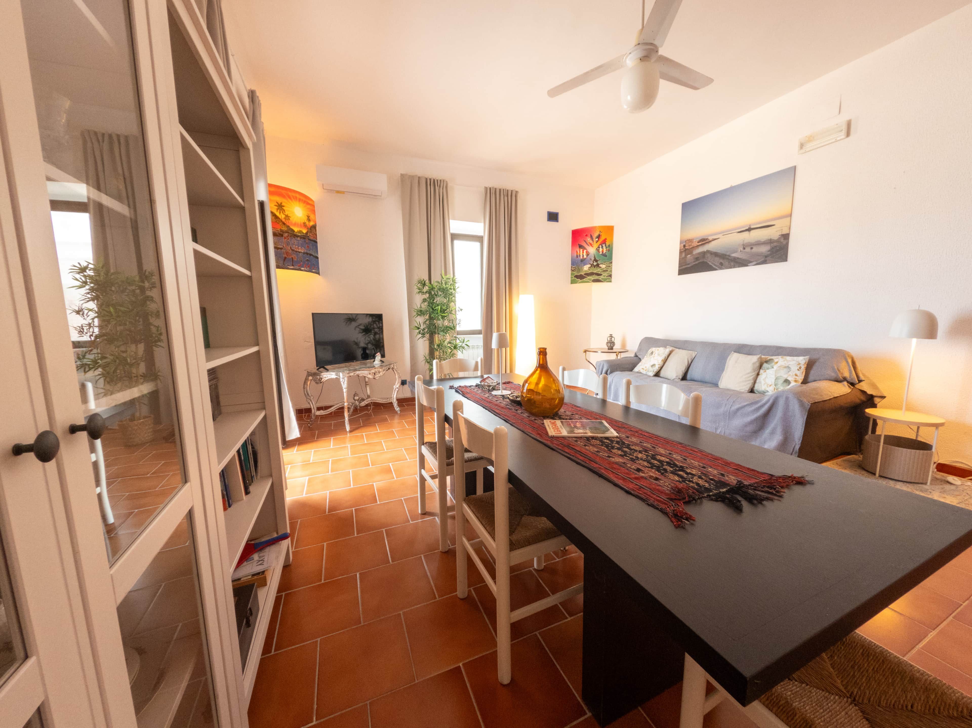 Una sala de estar moderna con comedor, sofá, televisor y ventilador de techo.