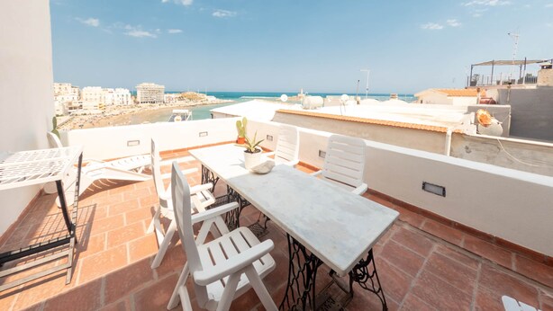 Una terrazza sul tetto con tavolo e sedie, una pianta in vaso e vista sulla spiaggia e sullo skyline della città.