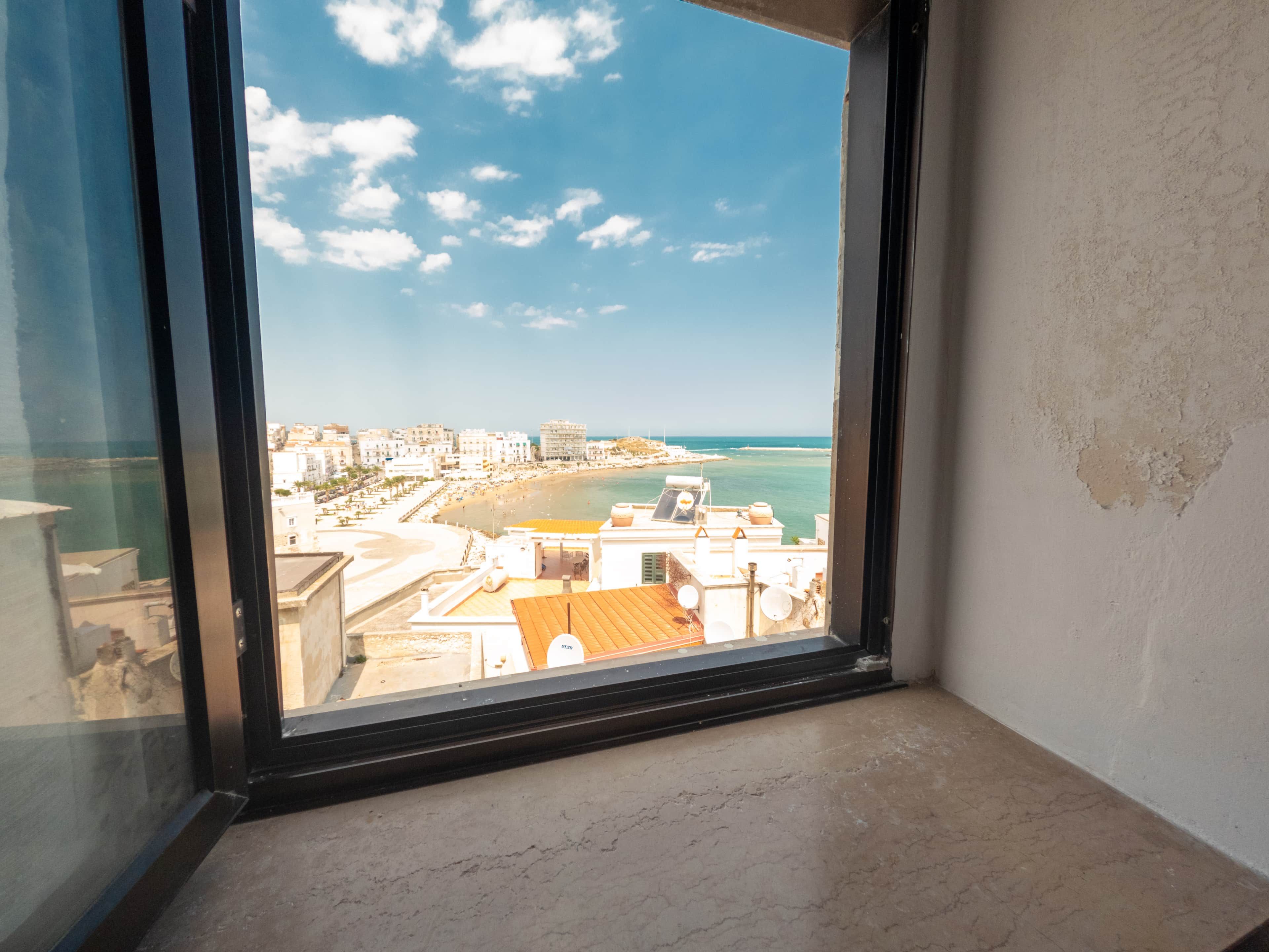 Una ventana con vistas a un paisaje urbano costero, que incluye edificios y una playa.