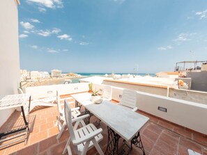 Une terrasse sur le toit, avec une table et des chaises, un pot de fleurs et une vue sur la plage et le paysage urbain.