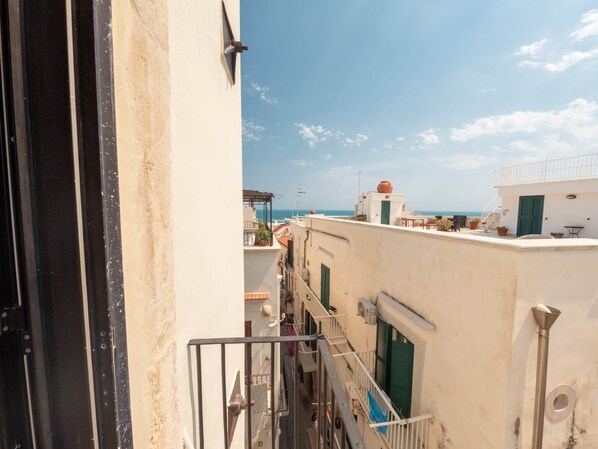 A narrow urban street with buildings, a visible balcony, and a clear sky.