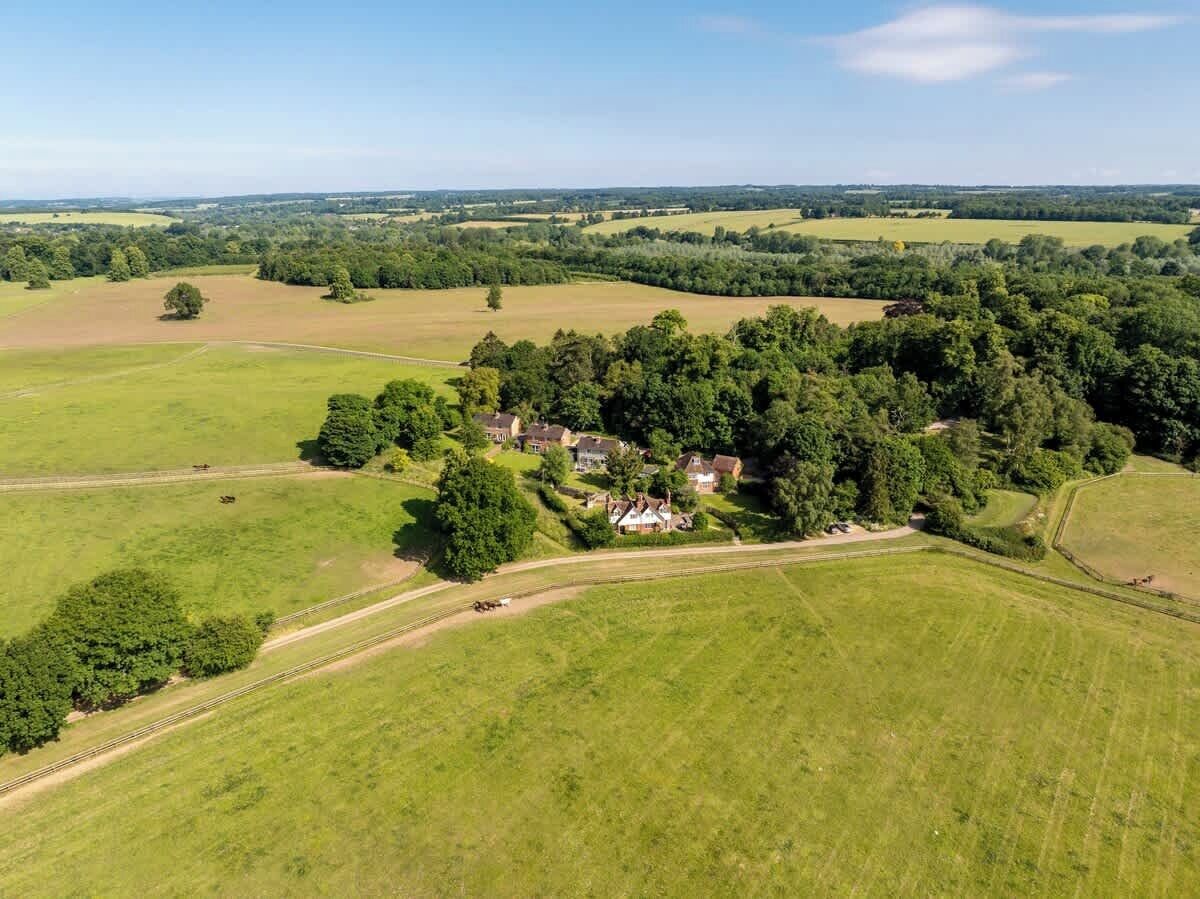Une vue aérienne d’une propriété rurale, avec un ensemble de maisons entourées de champs et d’arbres.