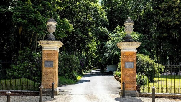A paved pathway leading through a gated entrance with two brick pillars topped with decorative urns, surrounded by lush greenery. - The Studio - A cosy studio apartment (Hungerford)