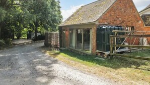A brick building with large windows, a gravel driveway, and a wooden gate. - The Studio - A cosy studio apartment (Hungerford)