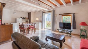 Una sala de estar con sofá, una mesa de centro, televisor y una zona de cocina con refrigerador y mesa de comedor.