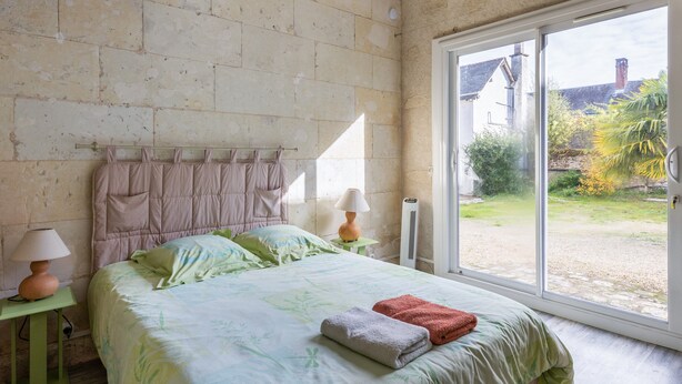Un dormitorio con cama, mesita de noche, lámpara, ventana y vistas al exterior.