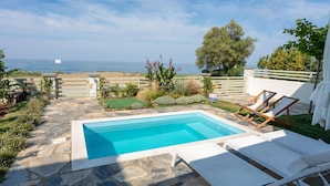 A pool with lounge chairs, a stone pathway, and a view of the sea. - Villas in Pelion (Zagora-Mouresi)