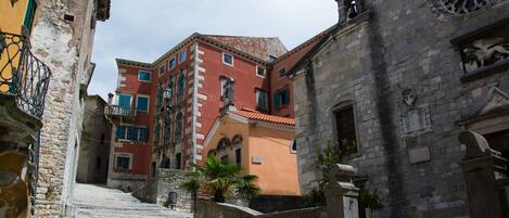 A narrow street with stone steps leading up to a building with a red facade and a clock tower.