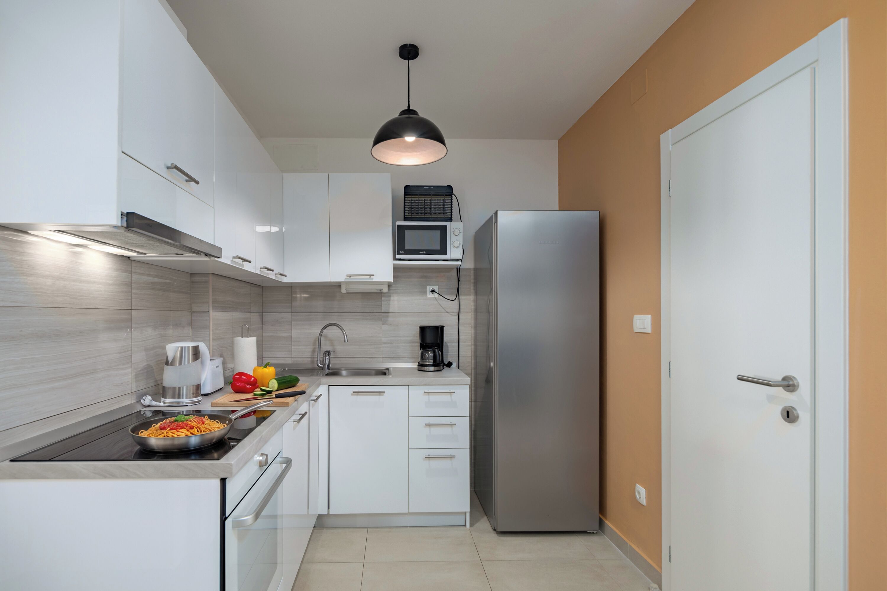 A modern kitchen with white cabinets, a stainless steel refrigerator, a microwave, and a kettle.