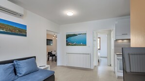 A modern living room with a sofa, a dining area, a kitchen, and a hallway leading to another room. - Seaview Pool House Mytilus (Rasa)