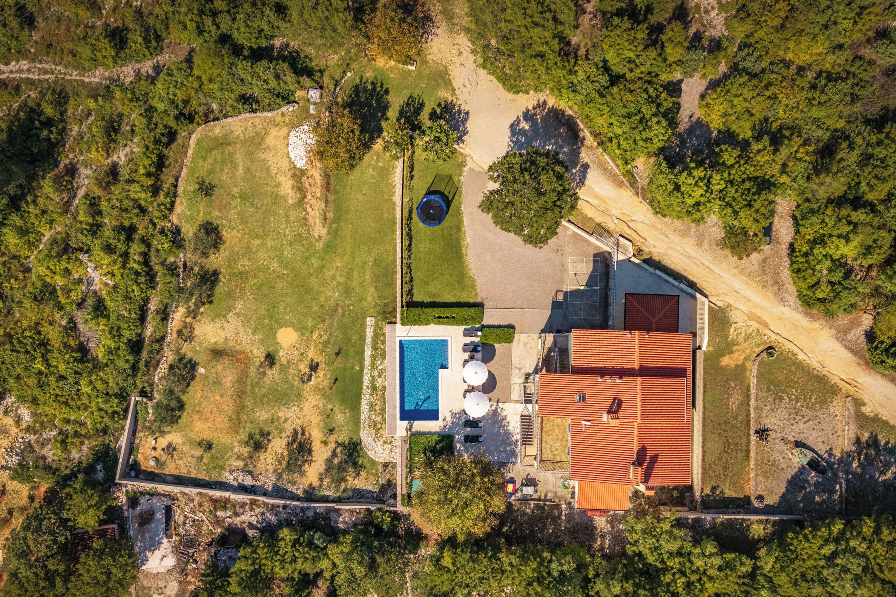 An aerial view of a property with a swimming pool, a red-roofed building, and a surrounding garden.