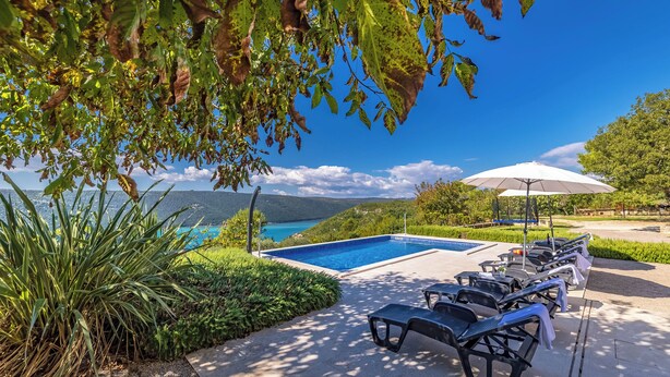A poolside area with lounge chairs and an umbrella, overlooking a clear blue sky and a distant view of mountains. - Seaview Pool House Mytilus (Rasa)