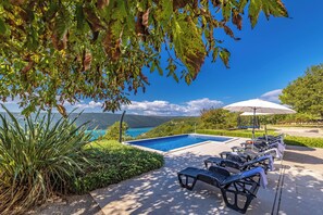 A poolside area with lounge chairs and an umbrella, overlooking a clear blue sky and a distant view of mountains. - Seaview Pool House Mytilus (Rasa)