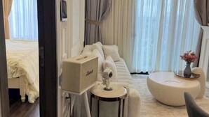 A modern hotel room with a large bed, a white sofa, a round coffee table, and a small side table. - X-Stay Luxe (Haiphong)