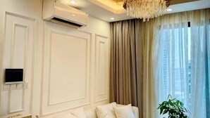 A hotel room with a white wall, air conditioning unit, a ceiling-mounted light fixture, and a large window with curtains. - X-Stay Luxe (Haiphong)