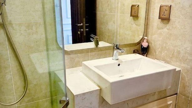 A bathroom with a glass shower enclosure, a white sink, and a mirror. - X-Stay Luxe (Haiphong)