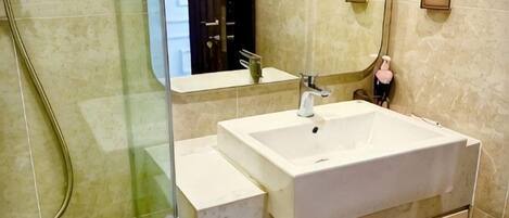 Un baño con cabina de ducha de vidrio, un lavabo blanco y un espejo.
