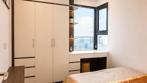 A bedroom with a bed, a desk, a wardrobe, and a window with a city view. - X-Stay Luxe (Haiphong)