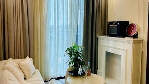 A living room with a sofa, a fireplace, a clock, and a plant. - X-Stay Luxe (Haiphong)