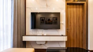 A modern hotel room with a flat-screen TV mounted on a marble wall, a wooden door, and a small desk with a chair. - X-Stay Luxe (Haiphong)