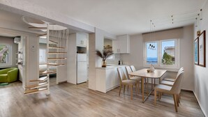 Eine moderne Küche mit weißen Schränken, ein Essbereich mit Tisch und Stühlen sowie Meerblick durch große Fenster.
