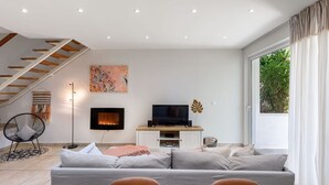 Ein modernes Wohnzimmer mit einer Couch, einem Fernseher, einem Kamin, einer Treppe und einem großen Fenster.