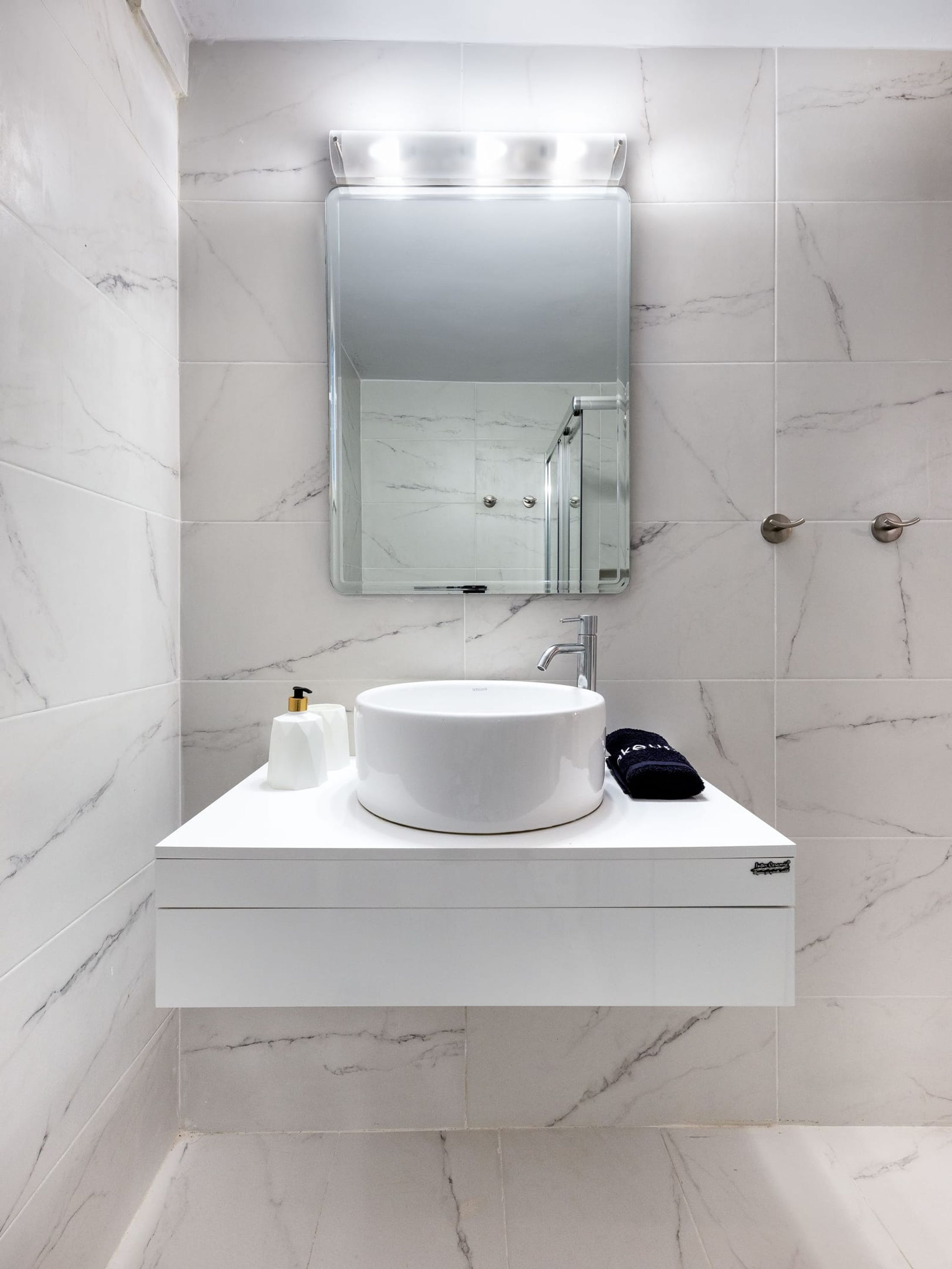 A bathroom with a white marble sink, a mirror above it, and a towel hanging on the wall.