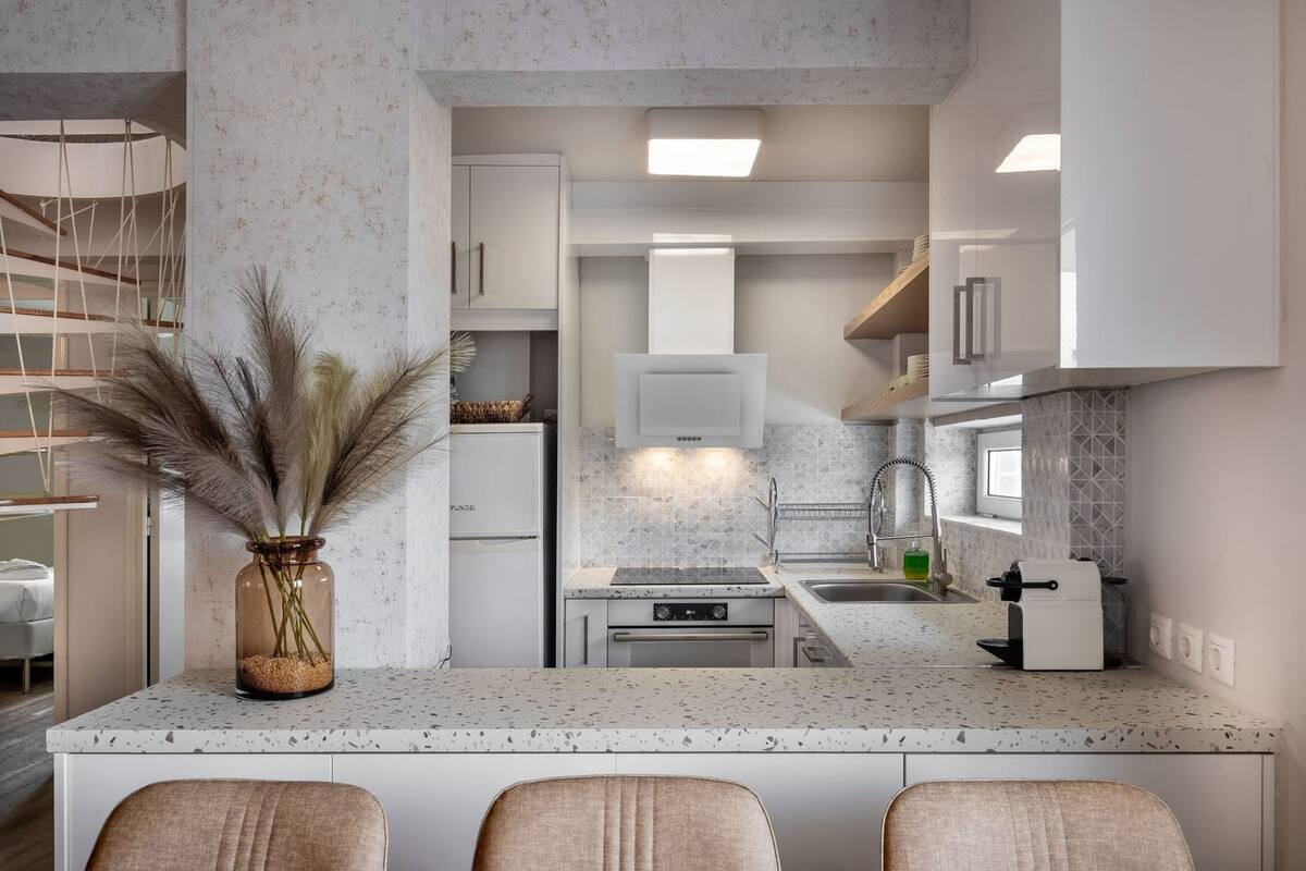 Una cocina moderna con una isla central, muebles blancos y una estufa integrada.