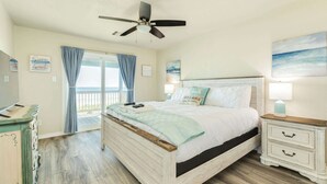 Un dormitorio con cama, mesita de noche, cómoda, ventilador de techo y ventana con cortinas.
