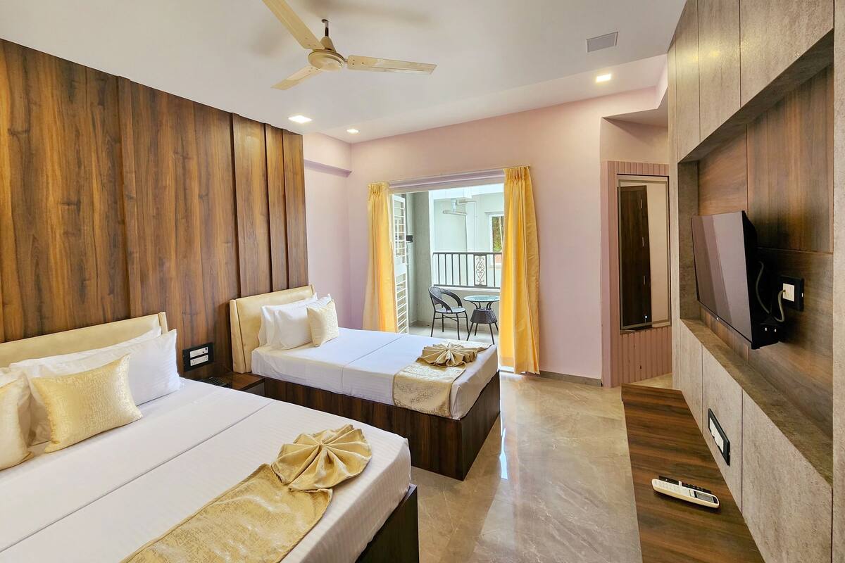 A hotel room with two beds, a ceiling fan, a TV, and a balcony with yellow curtains.