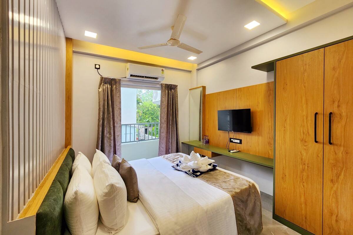 A hotel room with a bed, a TV, a wardrobe, and a balcony with curtains.